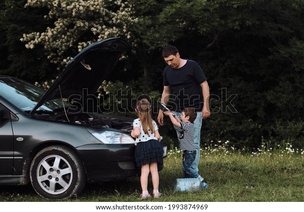Young mechanic dad teaches his\
son and daughter to repair car. Father opened the hood of car and\
shows children engine and spare parts. Spending time with\
father.