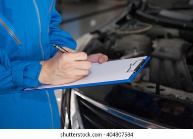 Young mechanic engineer taking a note on clipboard for examining a vehicle..