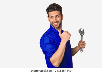 Young mechanic man holding a wrench points with thumb finger away, laughing and carefree. - Powered by Shutterstock