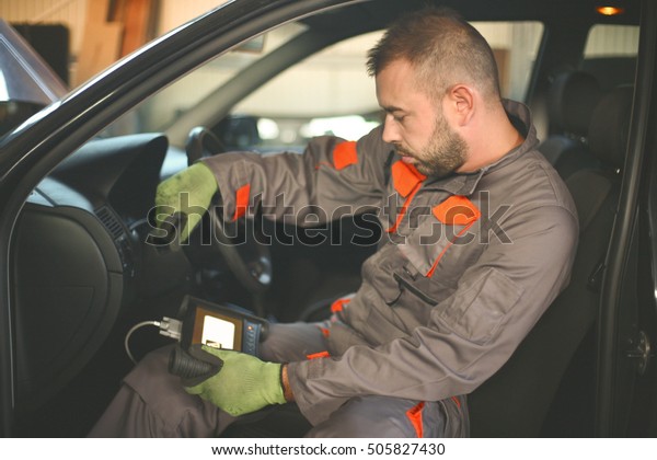 Young mechanic repair auto diagnostic on car in\
his workshop.
