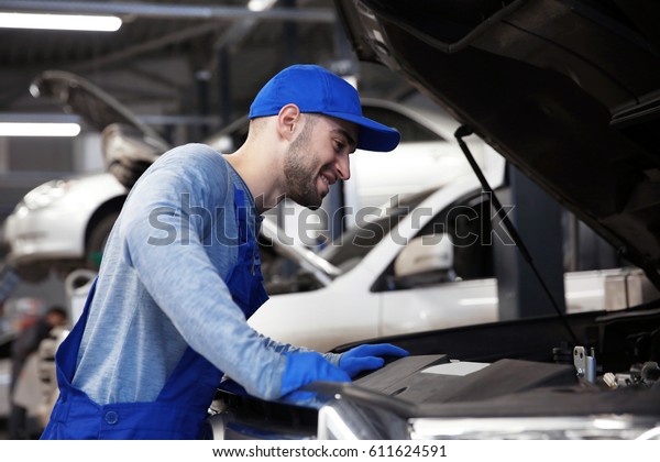 Young
mechanic standing in front of open car
hood