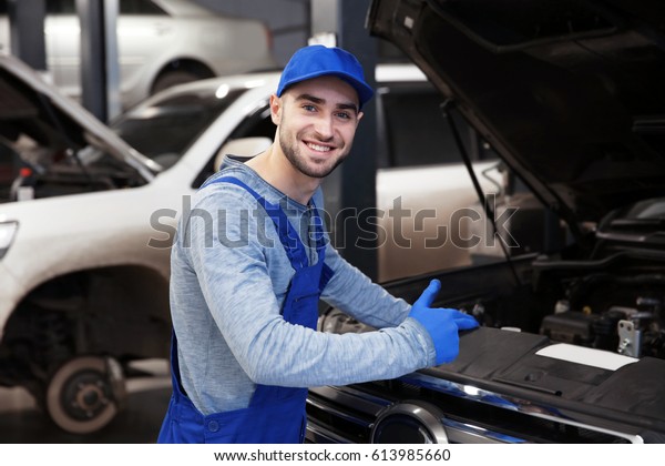 Young\
mechanic standing in front of open car\
hood