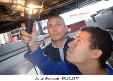 Young Mechanic Using Lamp To Inspect Vehicle Undercarriage