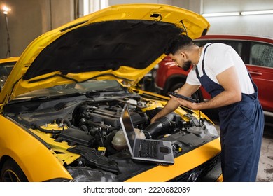 Young Mechanic Using Tablet Computer, Recording Automobile Engine Checks Collect Detailed Information During His Work On Car Workshop. Service Maintenance During Engine Repair.