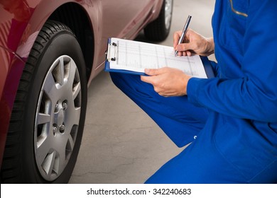 Young Mechanic Writing On Clipboard White Examining Car Wheel