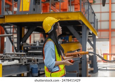 A young mechanical engineer is using a remote control to operate a crane or robot in a metal factory. Female technical worker is operating a metal production machine through a remote control - Powered by Shutterstock