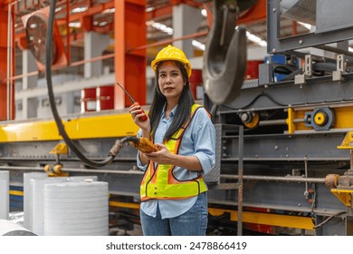 A young mechanical engineer is using a remote control to operate a crane or robot in a metal factory. Female technical worker is operating a metal production machine through a remote control - Powered by Shutterstock