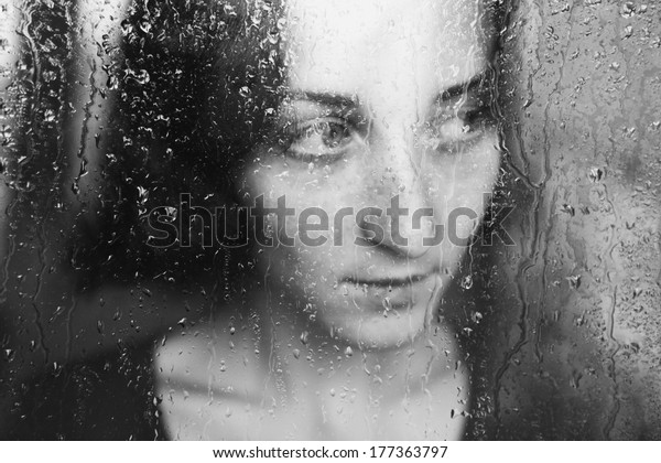 young melancholy and sad woman\
portrait  behind the window in the rain with rain drops on\
it