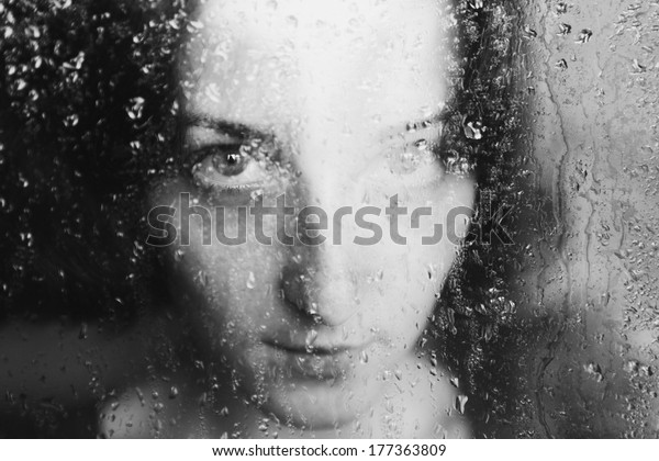 young melancholy and sad woman
portrait  behind the window in the rain with rain drops on
it