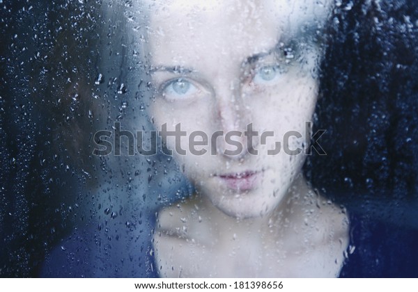 young melancholy and sad woman\
portrait behind the window in the rain with rain drops on\
it