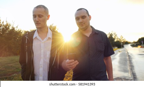 Young men have a serious talk while walking in the city during beautiful sunset with lense flare effects. Looking at mobile phone businessman showing something about new project, their work
