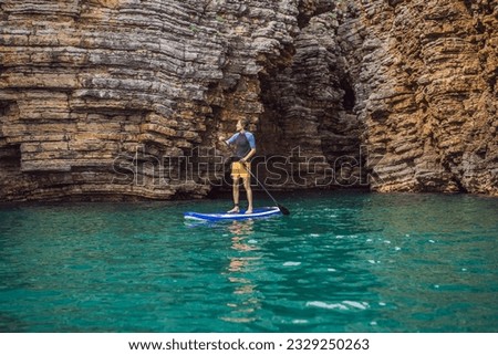 Young men Having Fun Stand Up Paddling in blue water seaamong the rocks in Montenegro. SUP