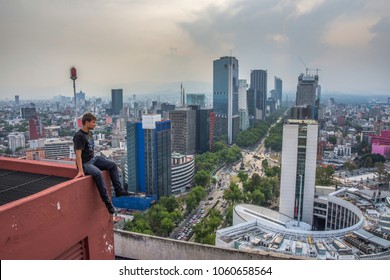 Young Men Sittingon The Rooftop Building In Mexico City. Paseo De La Reforma Panoramic View. Extreme Men On The Rooftop