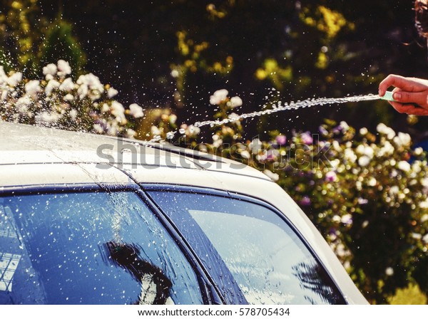 Young men washing silver car with pressured water
and brush at sunny day. Close up of cleaning car on summer time.
Taking care of the car. Man cleaning modern car with clear water in
the garden