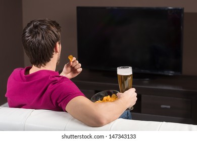 Young Men Watching TV. Rear View Of Young Men Drinking Beer And Eating Snacks While Watching TV