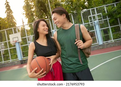Young men and woman playing basketball on playground on summer day. Couple playing basketball. Outdoor hobbies concept