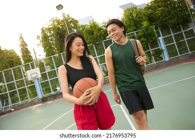 Young men and woman playing basketball on playground on summer day. Couple playing basketball. Outdoor hobbies concept