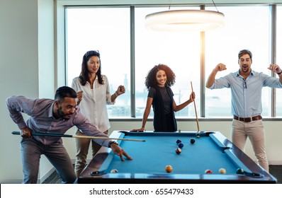 Young men and woman playing billiards at office after work. Business colleagues involving in recreational activity after work. - Powered by Shutterstock