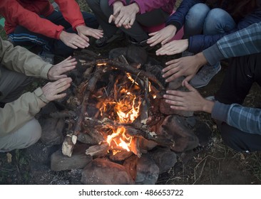 young men and women hands warm by the fire. They sit around the fire. Travel concept.  - Powered by Shutterstock