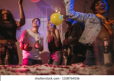 Young Men And Women Having Fun At A Colorful House Party With Decorations And Confetti All Around. Friends Dancing And Celebrating Holding Drinks At A House Party.