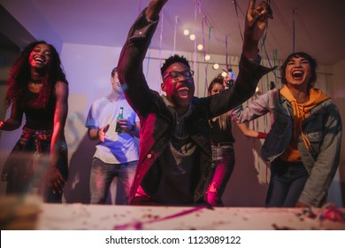 Young Men And Women Having Fun At A Colorful House Party. Friends Dancing And Shouting In Joy At A House Party.