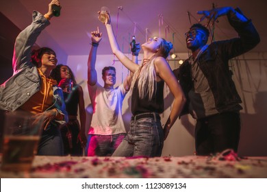 Young men and women having fun at a colorful house party. Friends dancing in joy holding drinks at a house party.