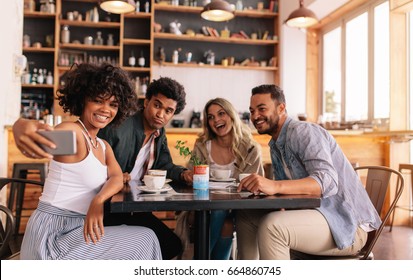 Young men and women sitting at cafe table and taking a self portrait on mobile phone. Diverse group of friends taking selfie on smart phone. - Powered by Shutterstock