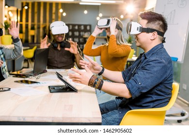 Young Men And Women Sitting At A Table With Virtual Reality Goggles. Multiethnical Business Team Testing Virtual Reality Headset In Office Meeting.