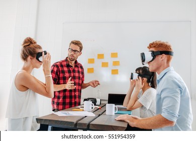 Young men and women sitting at a table with virtual reality goggles. Business team testing virtual reality headset in office meeting. - Powered by Shutterstock