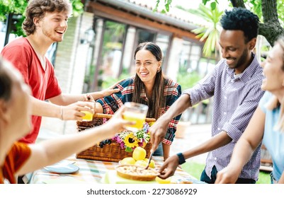 Young men and women toasting healthy orange fruit juice at farm house pic nic - Life style friendship concept with multicultural friends having fun together on afternoon relax time - Bright filter - Powered by Shutterstock