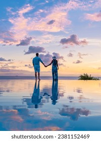 Young men and women watching the sunset with reflection in the infinity swimming pool at Saint Lucia Caribbean, couple at infinity pool during sunset on a luxury vacation at St Lucia