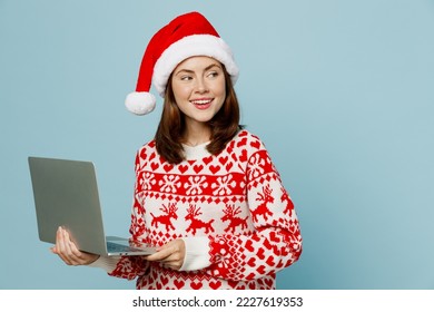 Young merry IT woman wear red sweater Santa hat posing hold use work on laptop pc computer look aside on area isolated on plain pastel light blue cyan background. Happy New Year 2023 holiday concept - Powered by Shutterstock