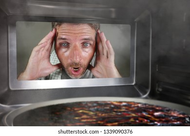 Young Messy And Funny Dummy Man In The Kitchen Looking Through Microwave Or Oven Pizza Burning Overcooked Making A Mess Of Home Cook In Domestic Disaster And Lifestyle Concept