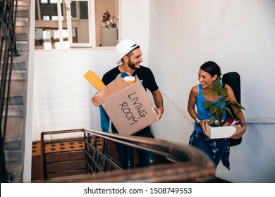 Young Mestizo Woman And Handsome Caucasian Man Moving In To New Apartment, Carrying Boxes On The Stairs Indoor.Smiling Happy Woman And Man  Student Couple Rent New Flat In College Campus