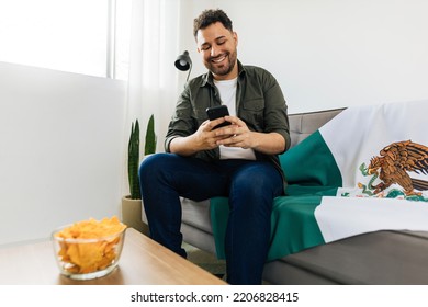 Young Mexican Man Using His Cell Phone To Invite Friends To Watch A Football Game At His Home.