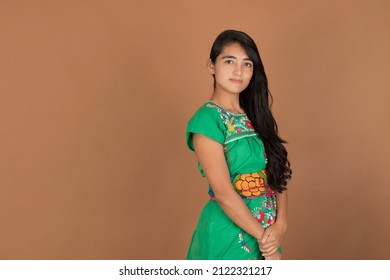 Young Mexican Woman Of Latina Ethnic Origin, Brunette, Long And Black Hair, Wearing A Green Maya Dress With Her Arms Crossed, Serious And Looking At The Camera