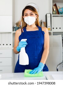 Young Mexican Woman In Medical Mask Cleaning Table With Spray At Company Office