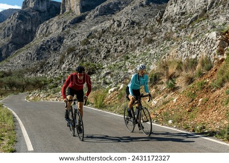 Young and Mid Adult Friends Cycling Up Rural Mountain Road, Alicante, Costa Blanca, Spain - stock photo