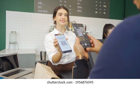 Young Middle East woman barista people in apron collecting an order payment by scanning QR code on phone screen, talking to customer at the counter, coffee shop cafe cashier. People lifestyle. Service - Powered by Shutterstock