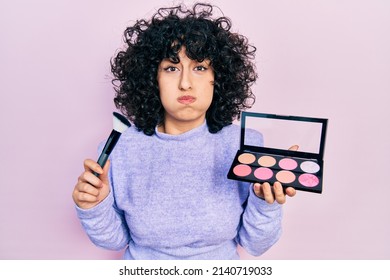 Young Middle East Woman Holding Makeup Brush And Blush Puffing Cheeks With Funny Face. Mouth Inflated With Air, Catching Air. 