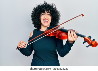 Young middle east woman playing violin smiling and laughing hard out loud because funny crazy joke.  - Powered by Shutterstock