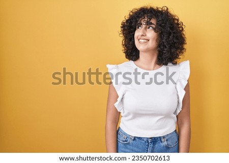 Young middle east woman standing over yellow background smiling looking to the side and staring away thinking. 