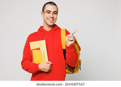 Young middle eastern man boy student wear red casual clothes backpack bag hold books point index finger aside on area isolated on plain solid white background. High school university college concept