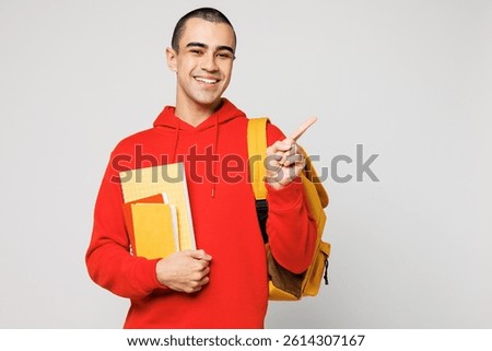 Young middle eastern man boy student wear red casual clothes backpack bag hold books point index finger aside on area isolated on plain solid white background. High school university college concept