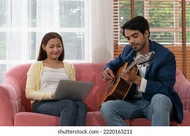 Young Middle Eastern Man Plaing Guitar While Asian Woman Working By Using Computer At Home