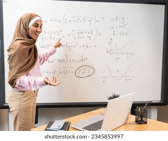 Young Middle Eastern teacher in a hijab explains a lesson online, pointing at the blackboard with math graphs and tasks. Creative Learning and Positive Learning Improves Student Achievement - Powered by Shutterstock