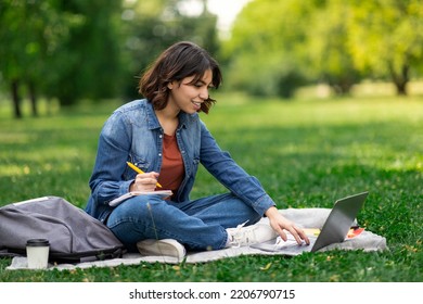 Young Middle Eastern Woman Study Outdoors With Laptop And Notepad Study Outdoors, Smiling Arab Female Student Preparing For Exam Outside, Sitting On Lawn In Park, Enjoying Online Education