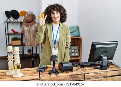 Young Middle Eastern Woman Working As Manager At Retail Boutique Showing And Pointing Up With Fingers Number Three While Smiling Confident And Happy. 