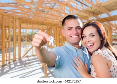 Young Military Couple On Site With House Keys Inside Their New Home Construction Framing.