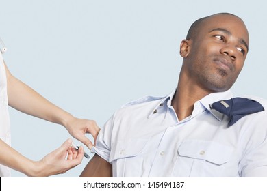 Young military man looking away as being injected by nurse over light blue background - Powered by Shutterstock